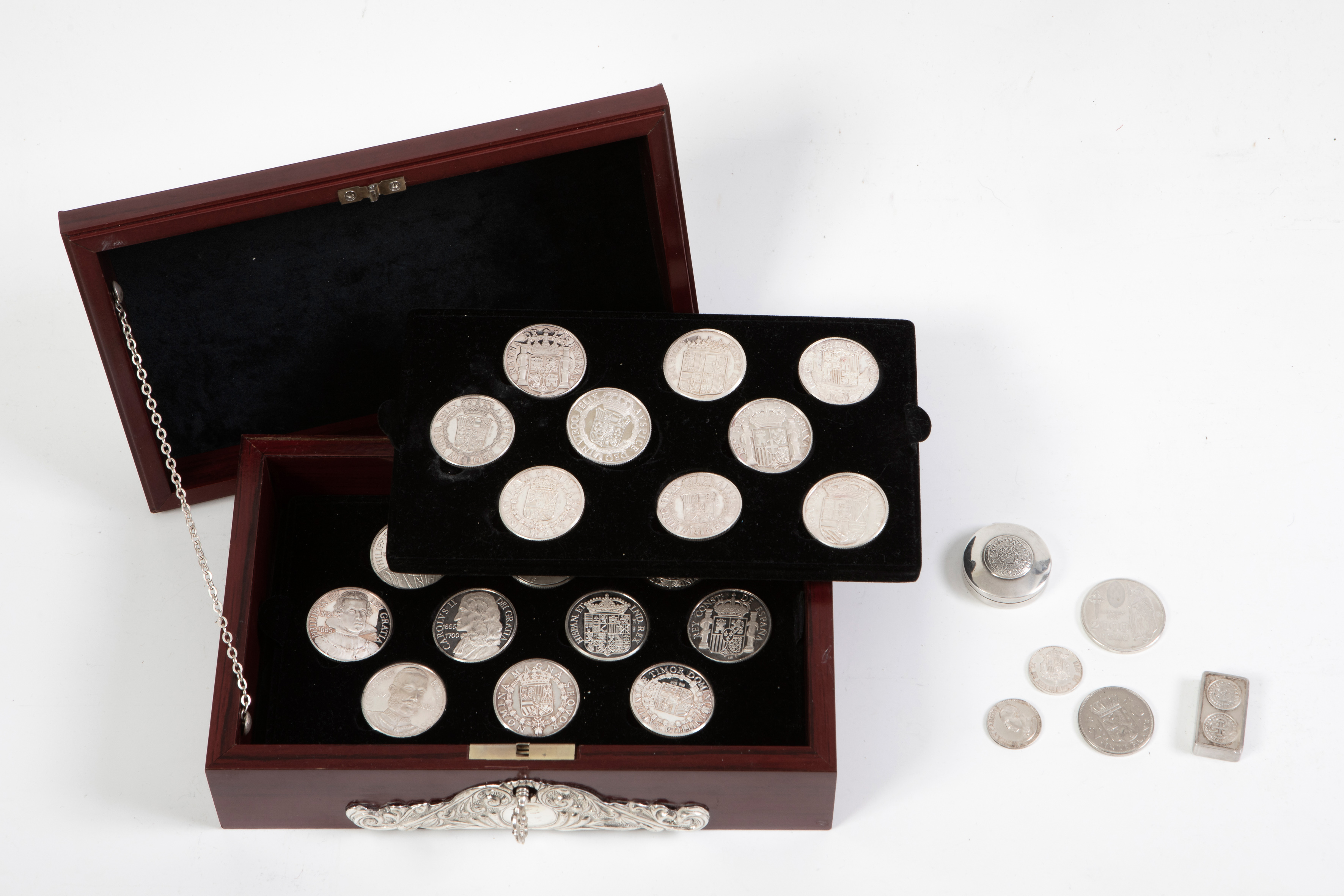 Caja en madera con monturas de plata con decoración repujada cuyo inerior contiene 19 monedas...