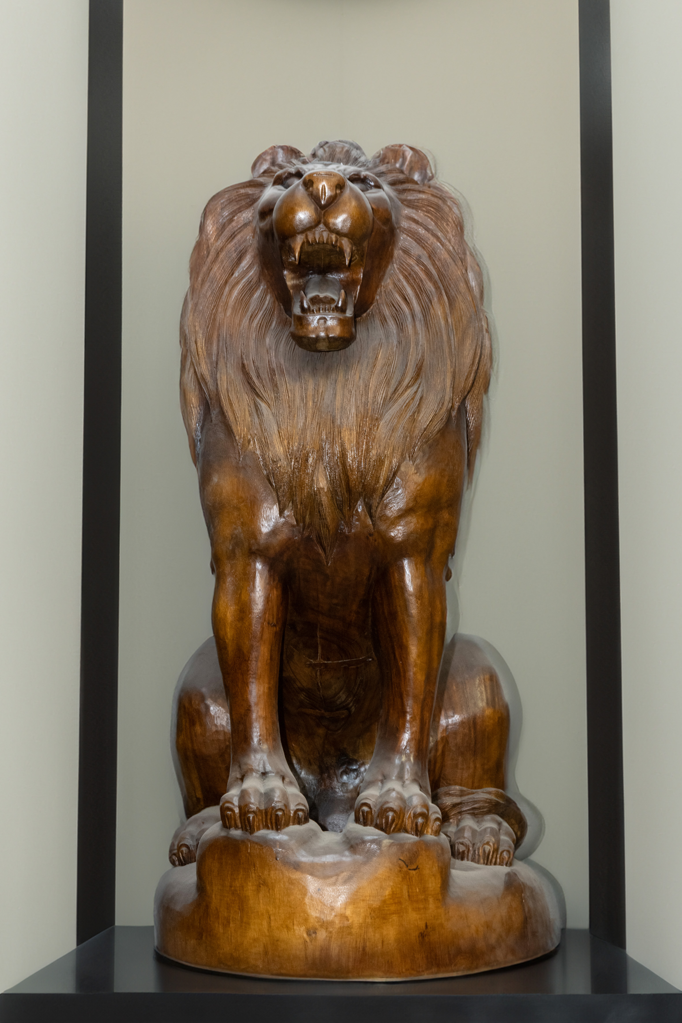 León; figura de animal sedente tallada, en fiera actitud, en madera exótica.
Altura: 130 cms