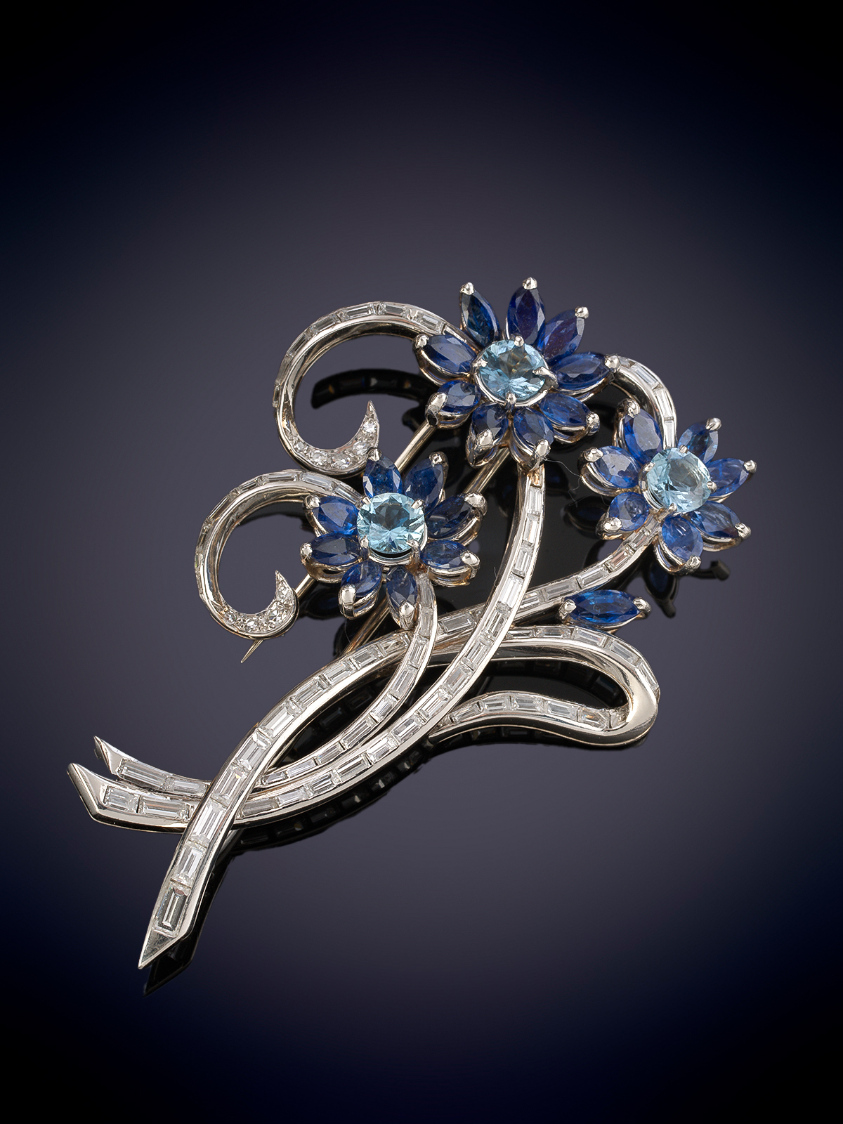 ELEGANTE BROCHE DE ZAFIROS EN FLOR Y DIAMANTES EN BAGETTE FORMANDO RAMAS. Montura en oro blanco 18k.